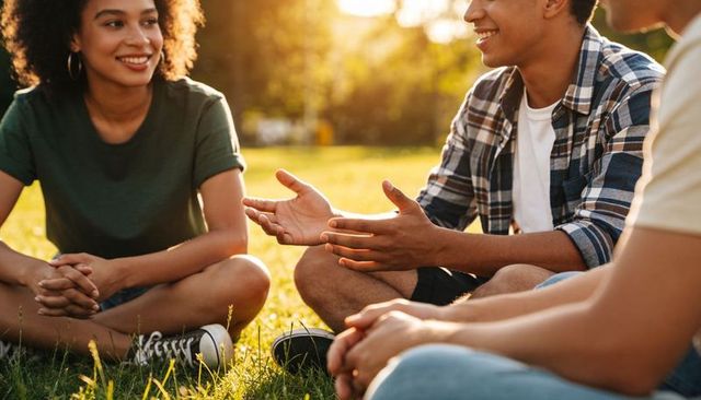 Young friends catching up on grass during golden hour, relaxed park conversation trio