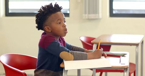 Focused African American Boy Writing in Classroom with Pencil