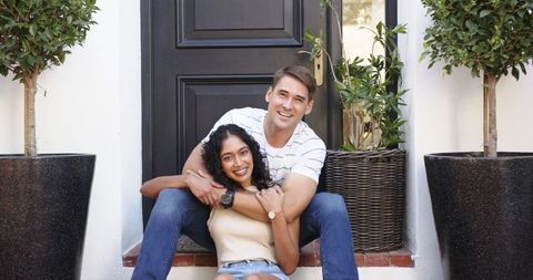 Diverse Couple Embracing on Home Steps Amid Potted Trees