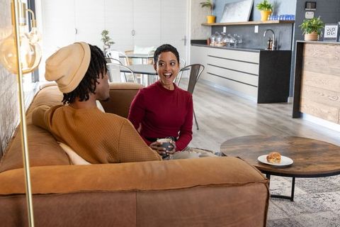 African american couple laughing and chatting on brown suede sofa in modern cozy open living space