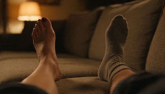 Couple relaxing on sofa stretching barefoot and sock closeup in warm cozy ambient light