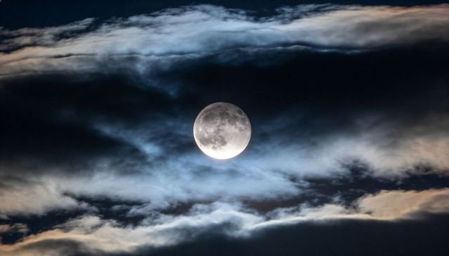 Moon glowing through layered clouds over night sky