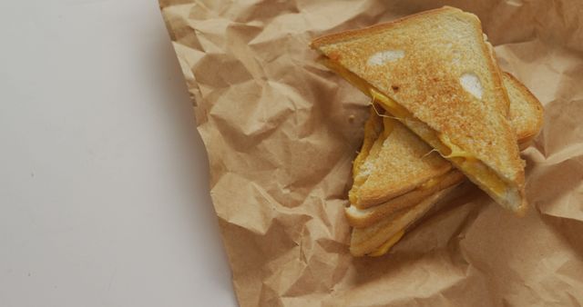Triangle-cut grilled cheese sandwich on crumpled brown paper, perfect for ads about comfort food, lunch specials, or cooking tutorials.