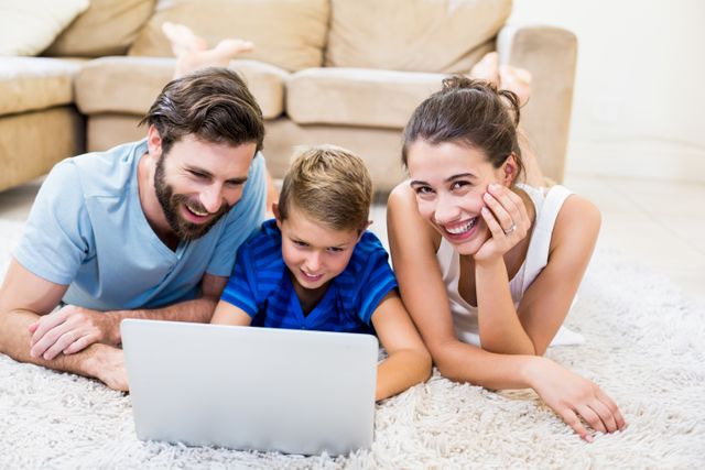 Parents and son lying on rug and using laptop at home