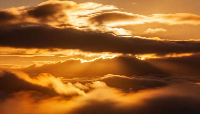 Golden crepuscular rays piercing layered cloud banks at dawn dramatic atmospheric light