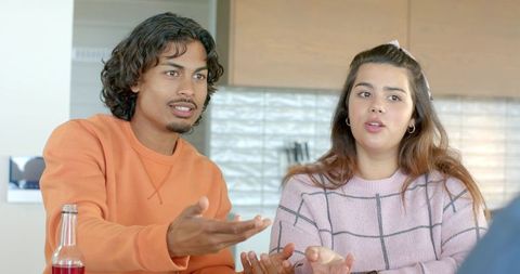 Young couple sitting at kitchen table, engaging in animated conversation and gesturing