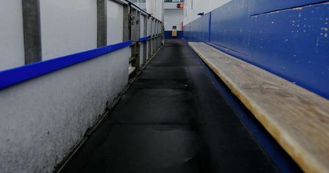 Empty hockey bench walkway leading along blue rink boards toward distant clock