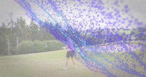 Mature woman standing on grassy hill in pink top and black shorts with purple-blue particle sweep