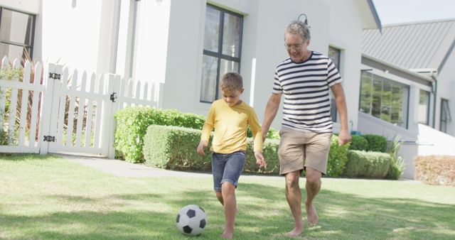 Grandfather and grandson playing soccer in front yard on a sunny day, smiling and bonding. Perfect for advertisements or articles on family time, health, and fitness. Suitable for content related to outdoor activities, family bonding, grandparents, and sport. Image evokes warmth, joy, and the importance of an active lifestyle.