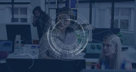 Focused team working at monitor with HUD data overlay in modern open office