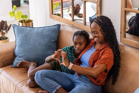 African mother and daughter sharing heart gesture on sofa, bonding at home with smartwatch