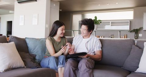 Couple reviewing tablet and signing documents on modern gray sofa in open-plan apartment