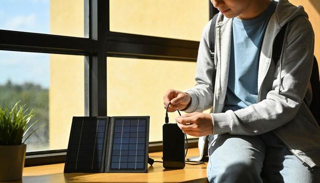 Teen charging power bank with foldable solar panel on windowsill, sustainable gadget