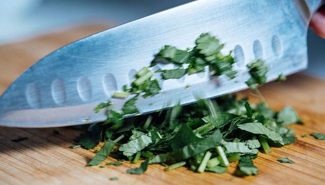 Chopping fresh herbs with stainless steel chef knife on wooden cutting board close-up