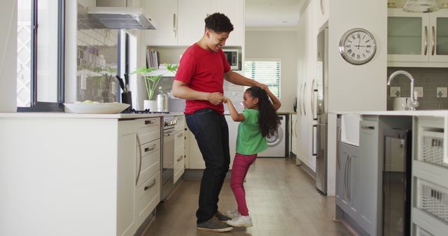 Father and daughter dancing together in modern kitchen, capturing a moment of family bonding and happiness. This image is ideal for marketing family-oriented products, blogs on parenting and home life, or advertisements focusing on family joy and togetherness.