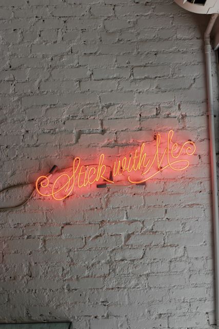 Illuminated red neon sign on textured white brick wall displaying the phrase 'Stick with Me'. Ideal for use in advertisements, social media posts, or blogs about motivation, companionship, interior decoration, or vintage decor. Captures a modern yet retro vibe, making it suitable for promotional materials or inspirational content.