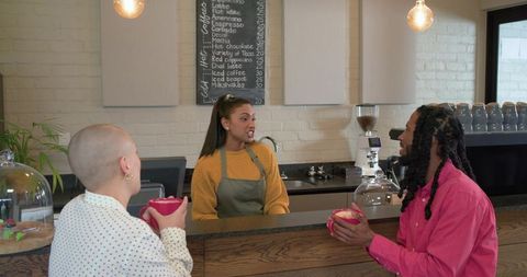 Indian barista engaging with diverse customers at cozy cafe counter with pink cups