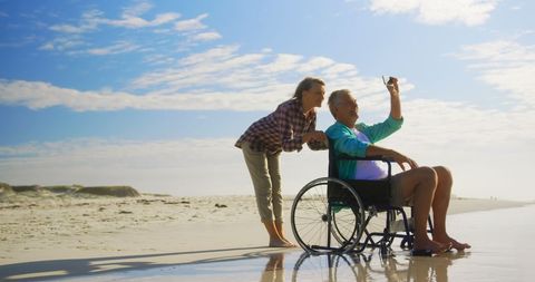 Senior Couple Taking Selfie on Beach in Wheelchair on Sunny Day