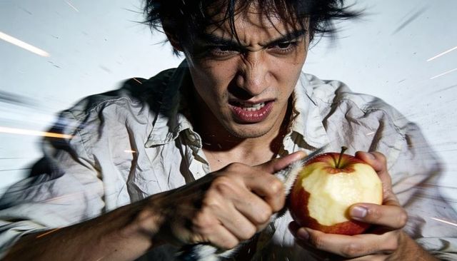 Intense asian man scraping apple with serrated knife, sparks flying and cinematic motion blur