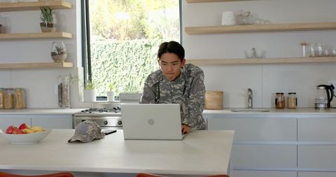 Young Soldier Engaged in Laptop Work in Sleek Home Kitchen