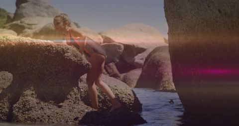 Girl climbing sunlit granite boulders and wading tide pools in striped swimsuit at rocky coast