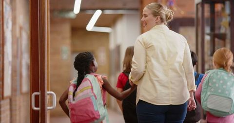 Female Teacher Guiding Elementary Students Through School Hallway