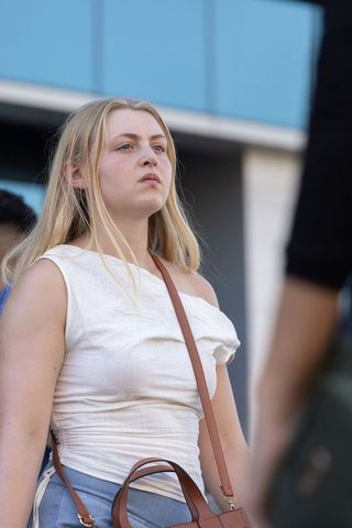 Young woman looking up by modern blue glass facade in off-white top with crossbody bag