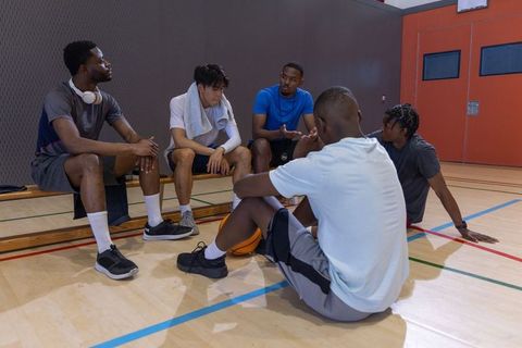 Diverse basketball teammates discussing strategy during timeout on indoor court