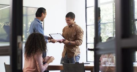 Colleagues applauding award presentation in office setting