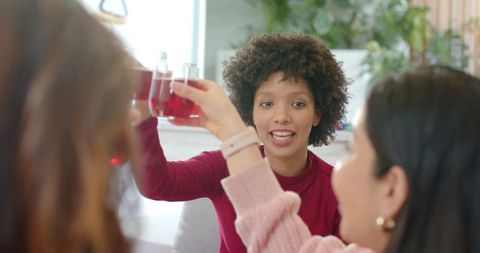 Multiracial friends toasting with red drinks on couch, celebrating cozy home gathering