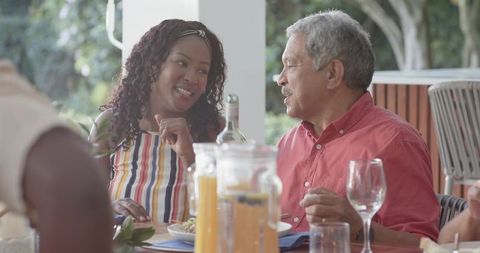 Sharing laughter at intergenerational outdoor brunch on sunlit patio, casual convivial dining