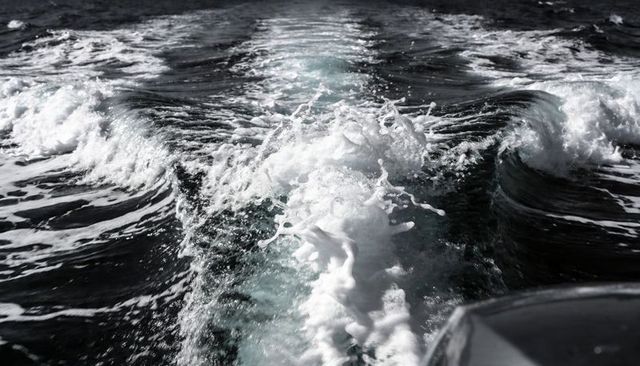 Boat wake churning foamy water and spray stretching toward horizon from stern transom