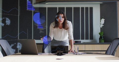 Woman presenting data in modern boardroom with laptop and tablet for corporate meeting
