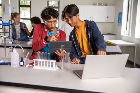 Diverse teens studying science using tablet and laptop in collaborative high school lab