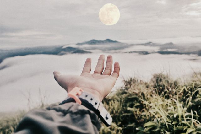 View of hand against landscape with mountains and moon in the sky. Nature, travel and adventure concept