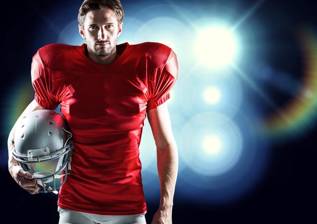 American football player wearing red jersey holding helmet, standing against illuminated blue background. Ideal for sports promotions, athletic advertisements, football team posters, and motivational content.