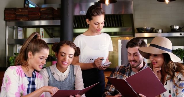 A diverse group of young adults is examining a menu in a restaurant, with a waitress ready to take their order, with copy space. Their engagement and varied expressions suggest they are making careful selections for their meal.
