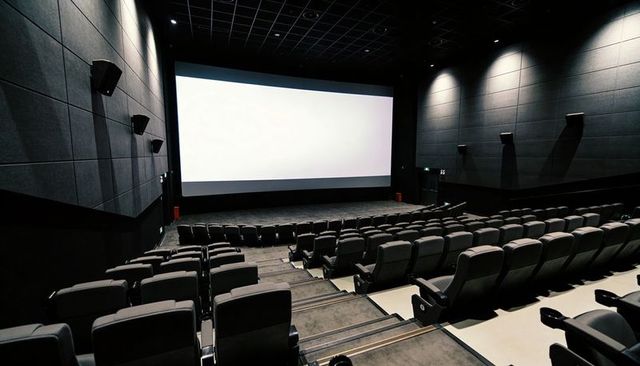 Empty modern cinema auditorium with large blank screen and reclining seats, dark interiors
