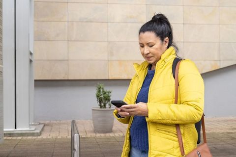 Middle-aged woman checking smartphone outside urban building in yellow puffer coat