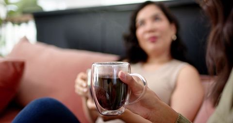 Sharing coffee on pink sofa: diverse women chatting casually with double-walled glass mug