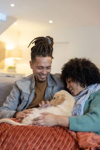 African american couple cuddling golden retriever puppy on couch in cozy living room