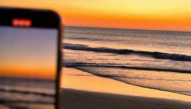 Blurry phone recording sunrise over calm sea with red rec indicator and golden reflections