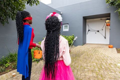 African american girls trick-or-treating as superhero and princess in suburban neighborhood