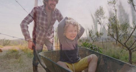 Father Joyfully Pushing Son in Wheelbarrow Through Orchard