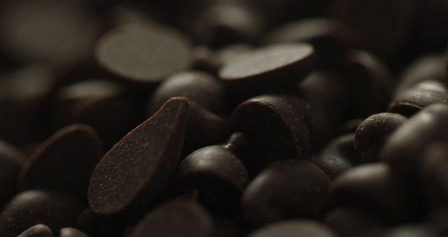 Dark chocolate chips scattered closely together create a rich and indulgent mood. Perfect for illustrating dessert-specific content, food blogs, or baking advertisements. The shallow depth of field emphasizes the texture and luxury of chocolate, ideal for upscale culinary uses.