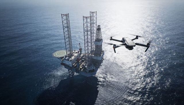 Quadcopter drone surveying offshore oil platform with helipad and sea reflections