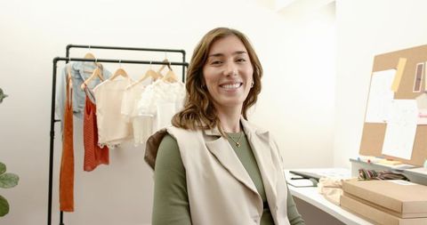 Smiling boutique owner styling garments on rack in bright minimalist fashion studio