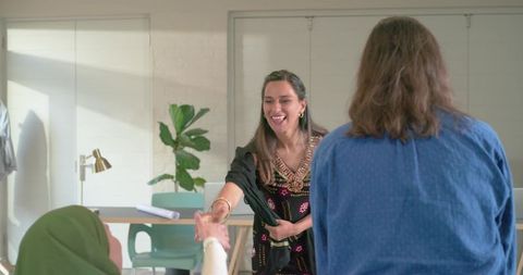 Women greeting with handshake in modern office, indian woman in embroidered tunic smiling