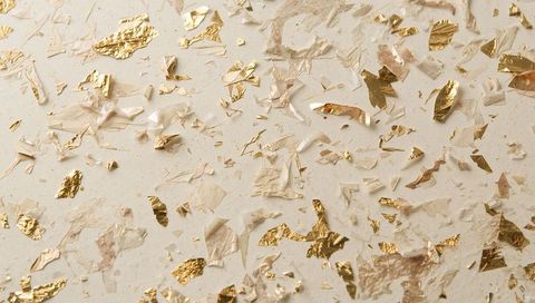 Gold leaf flakes scattering across cream craft paper with sheer tissue and foil