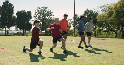 Diverse male team lunging through cones during outdoor warmup training on grass field